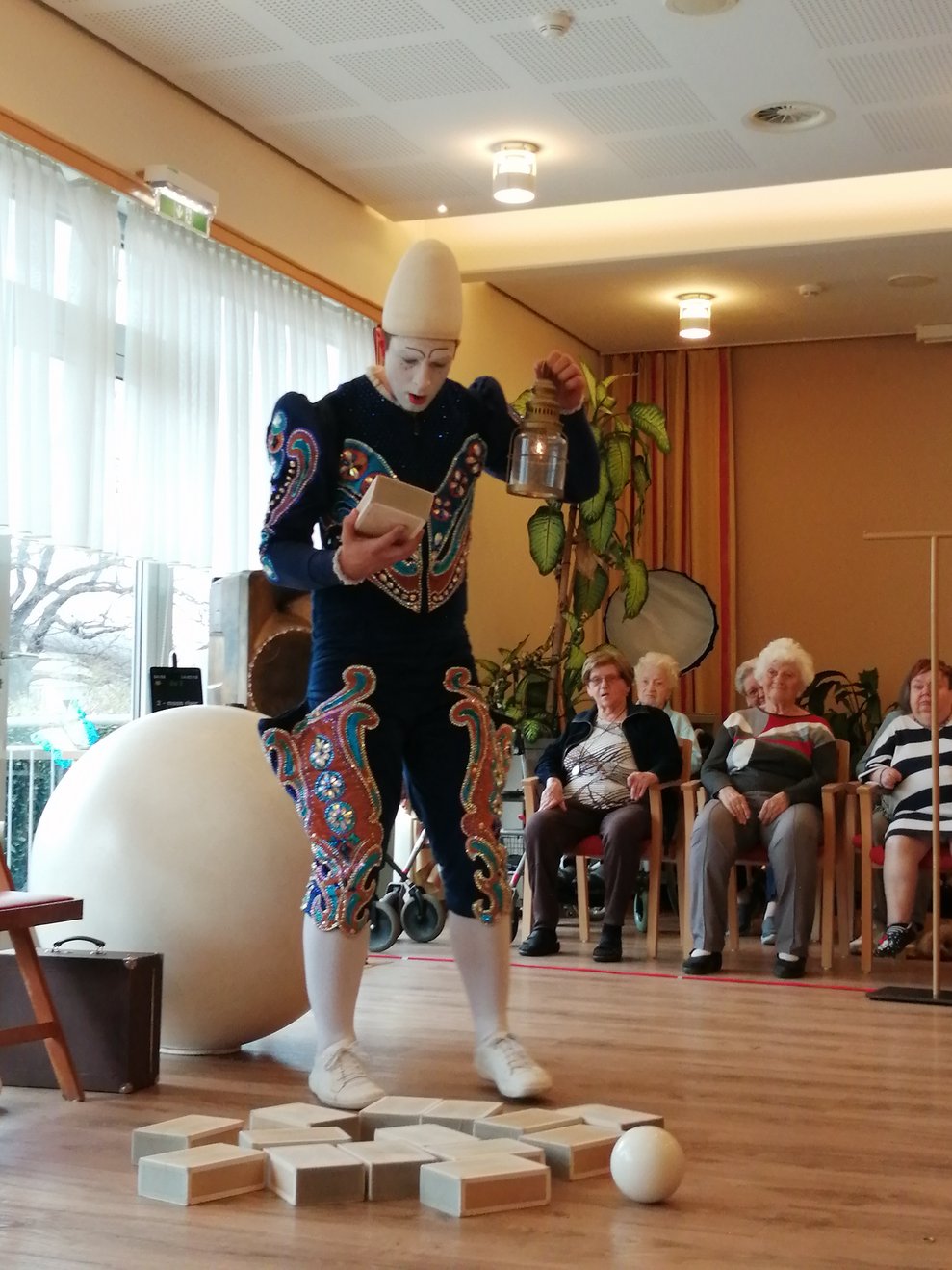Der Weißclown hält einen Holzklotz in einer und eine Laterne in der anderen Hand.