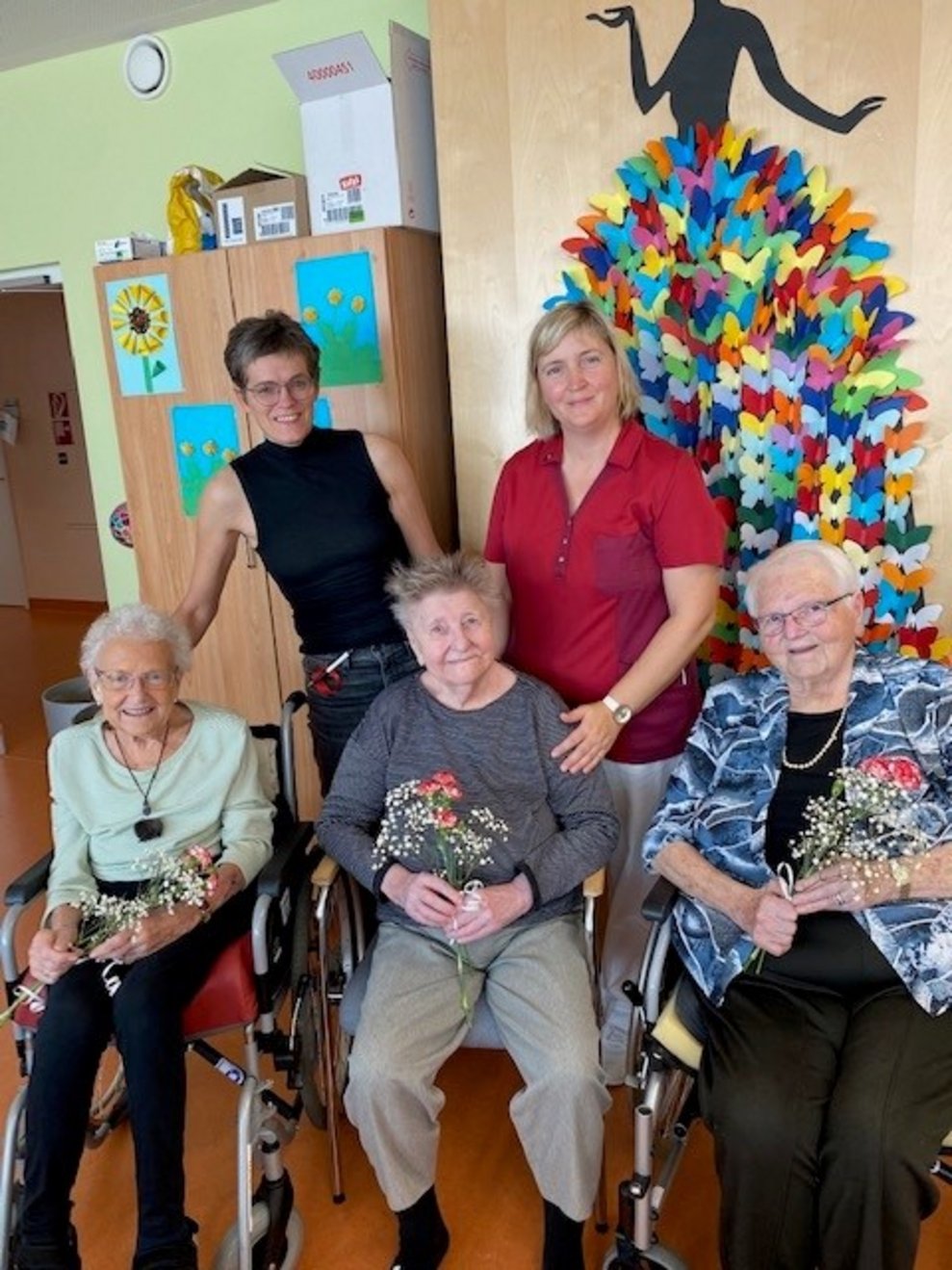 drei Bewohnerinnen halten eine Blume in der Hand als Geburts