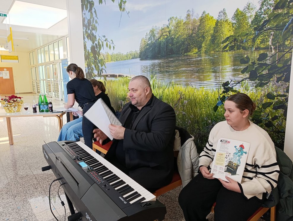 Mann blättert im Musikheft. Mädchen sitzt daneben. Keyboard steht da.