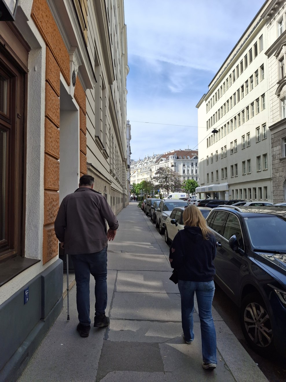 ein Mann und eine Frau gehen in Wien am Gehsteig, man sieht sie von hinten