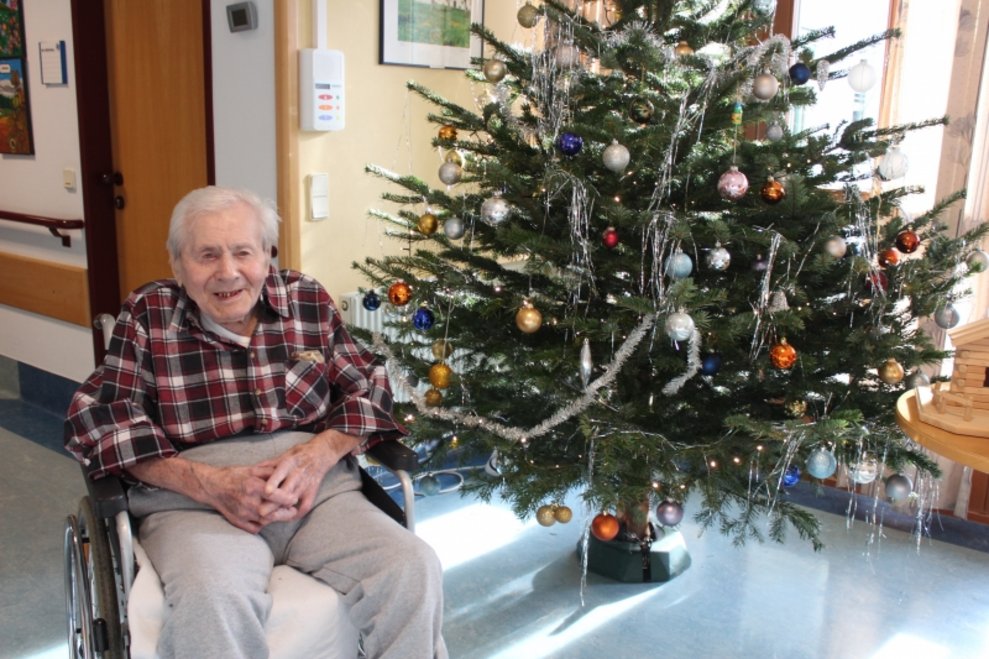 Ein Bewohner sitzt neben einem Christbaum.