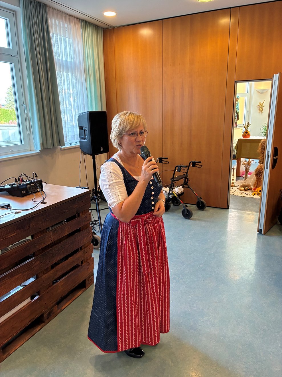 Pflegedirektorin im Dirndl steht und spricht ins Mikrofon. Mikrofon in der Hand.