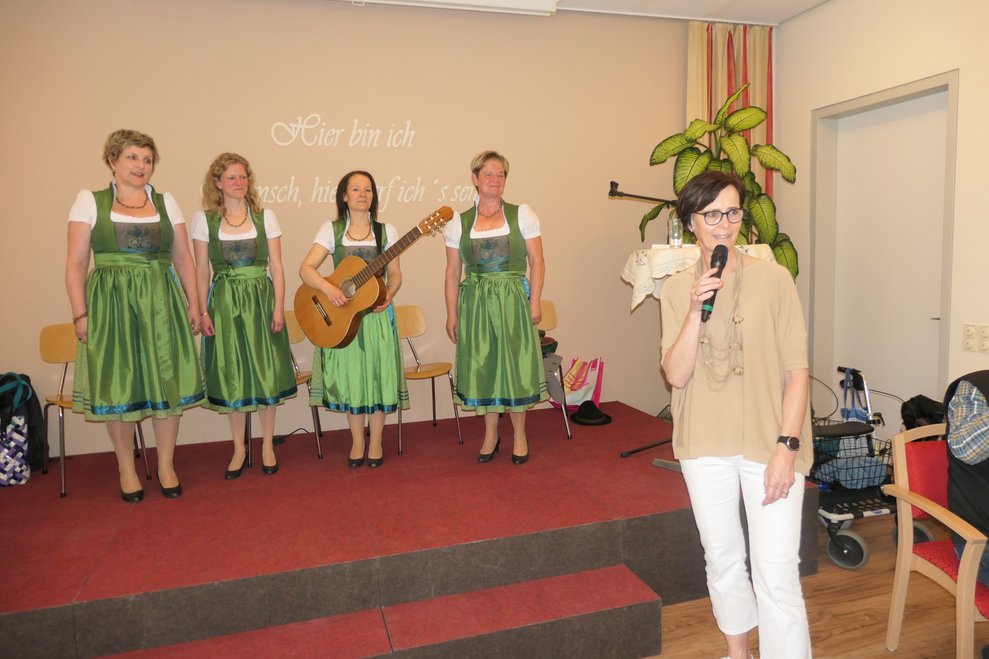 Eine Dame mit Mikrofon, im Hintergrund drei Damen im Dirndl auf der Bühne.