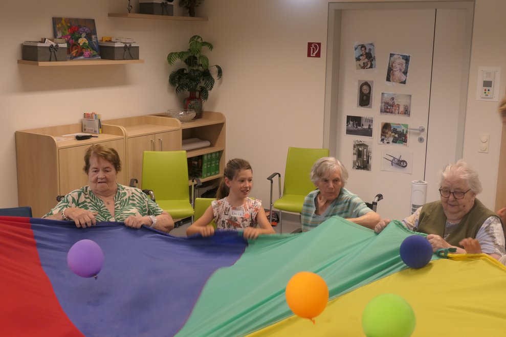 Die Kinder und SeniorInnen spielen mit dem Fallschirm und Luftballon.