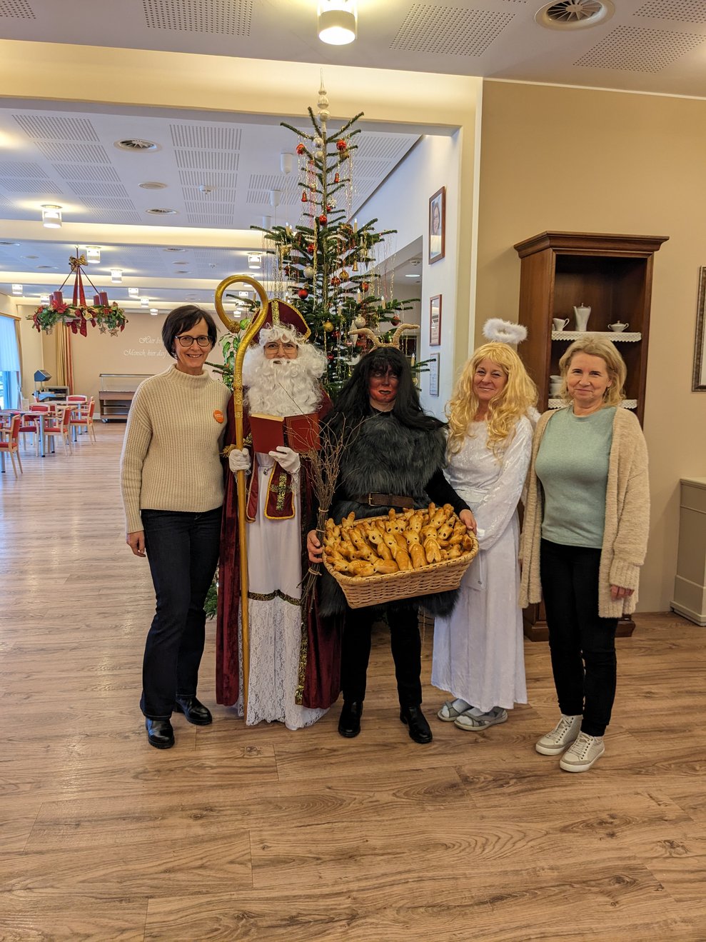 Nikolo, Krampus, Christkind die Direktorin und ihre Stellvertreterin vorm Christbaum.