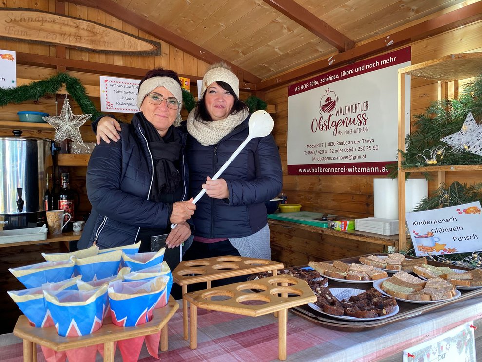 zwei Frauen stehen in der Punschhütte mit einem Kochlöffel in der Hand