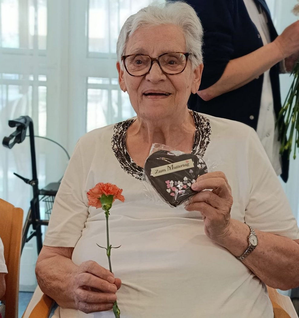 Bewohnerin hält verpacktes Schokomuttertagsherz und Nelke in den Händen.