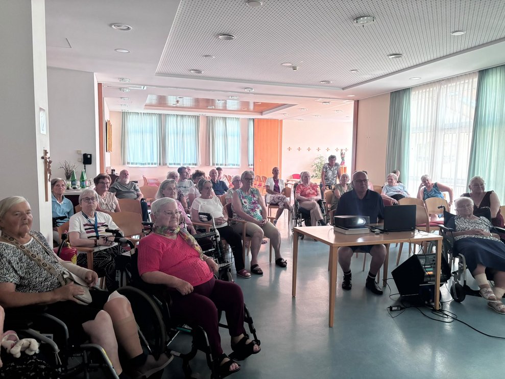 Sitzende Personen. Tisch mit Computer und Beamer. Mann bedient Computer.