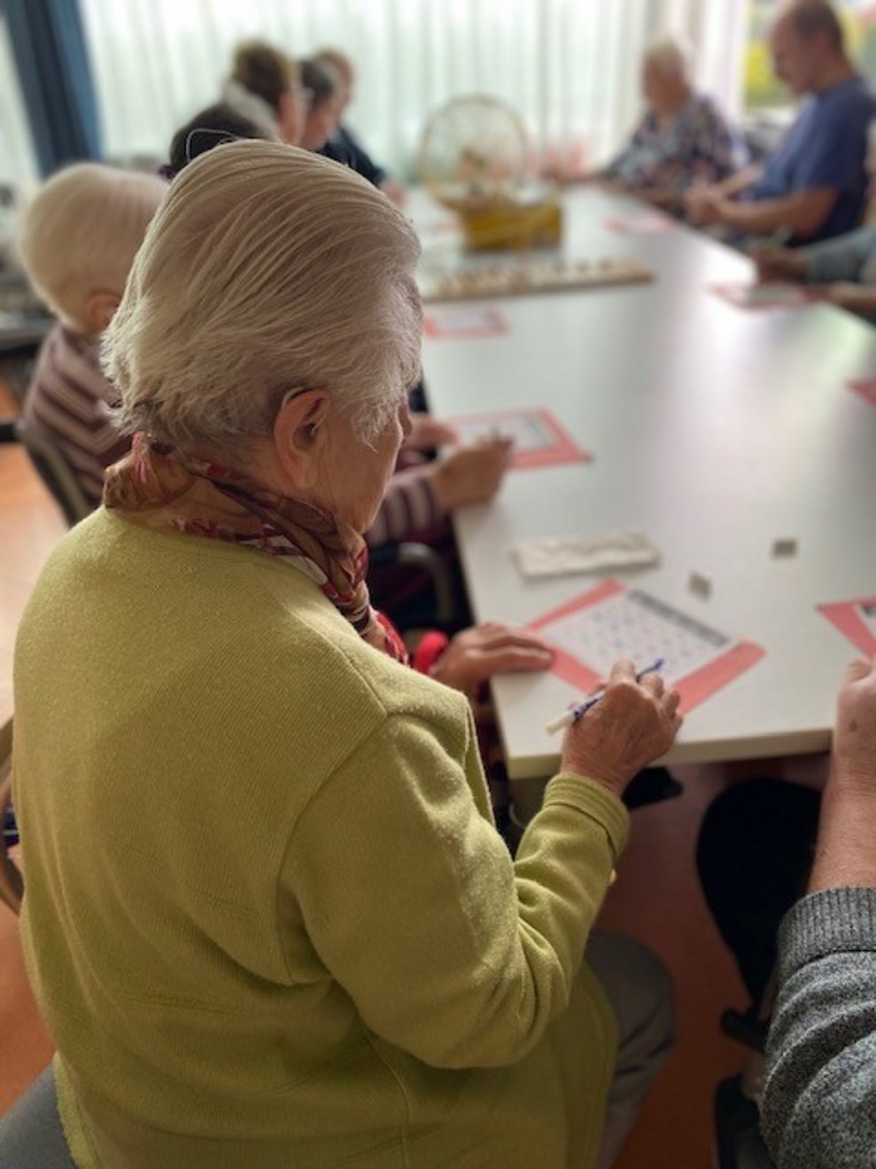 Bewohnerin sitzt beim Tisch und macht ein Kreuz bei einer Zahl
