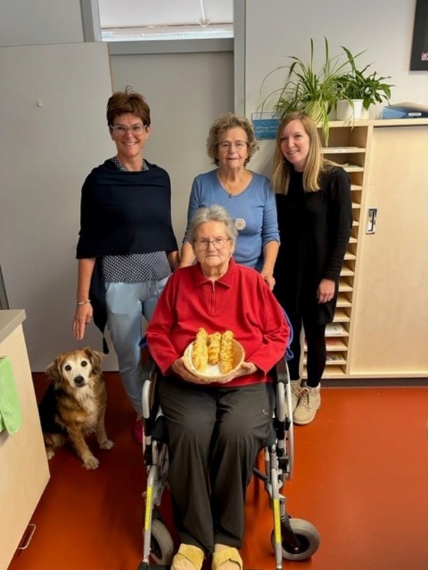 3 Frauen stehend, eine Frau im Rollstuhl mit Striezel in der Hand