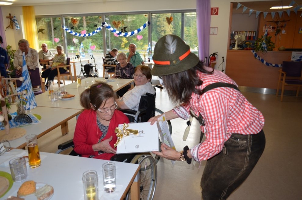 Eine Betreuerin übergibt eine Schachtel Pralinen an eine Bewohnerin.