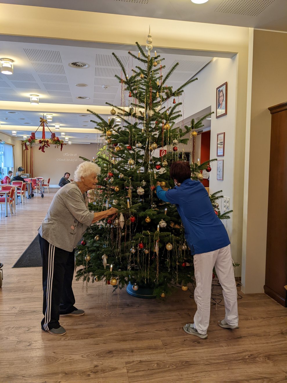 Zwei Damen schmücken einen Zimmerhohen Christbaum.