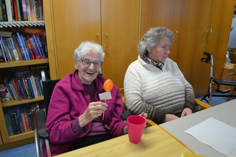 Eine Dame hält ein Osterei in der Hand, eine zweite Dame sitzt daneben
