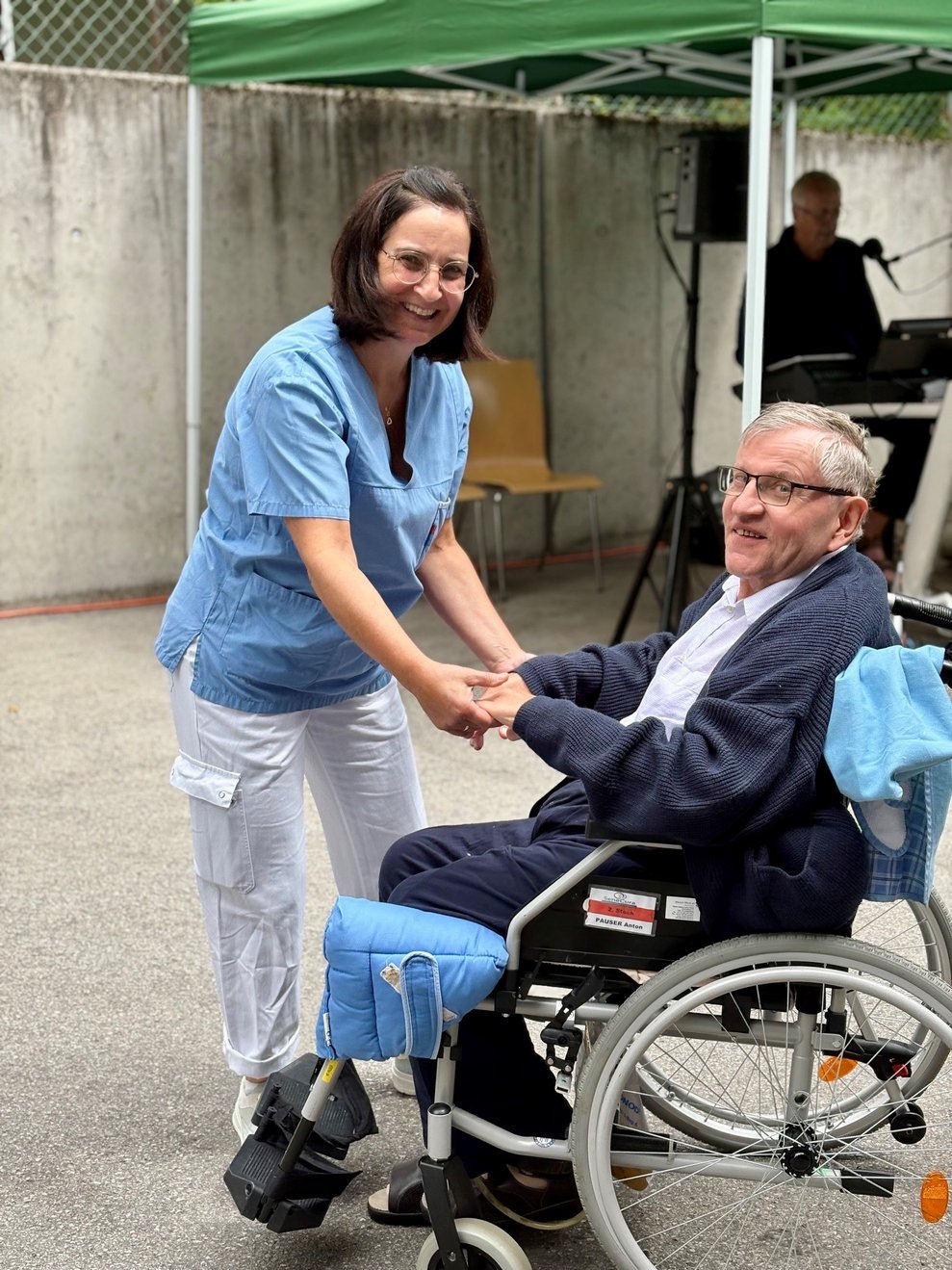 Eine Mitarbeiterin tanzt mit einem Bewohner, der im Rollstuhl sitzt.