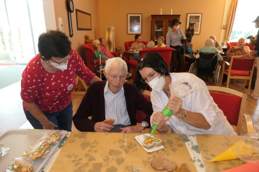 Zwei Damen und ein Herr verzieren ein Lebkuchenherz mit Zuckerguss.