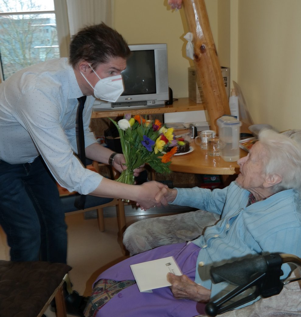 Der Direktor überreicht einer Bewohnerin Blumen.