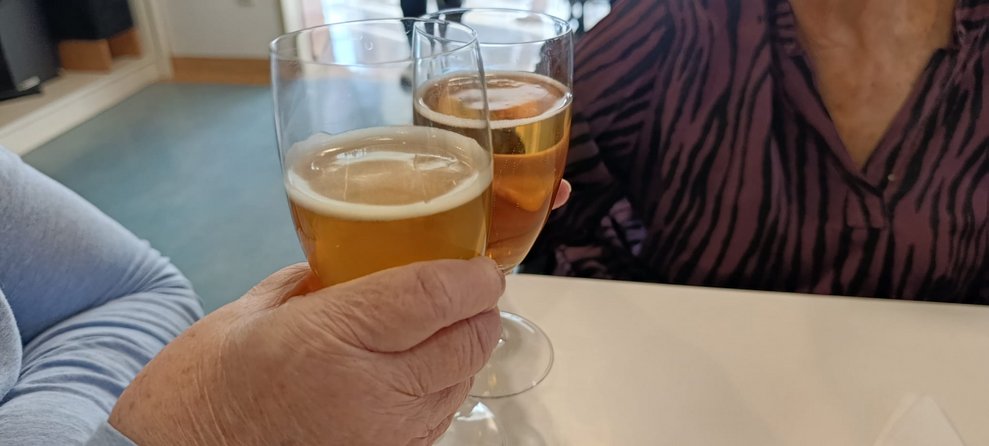 Zwei Hände halten jeweils zwei Gläser gefüllt mit Weißbier. (Zwei Gläser mit Weißbier stehen auf Tisch).