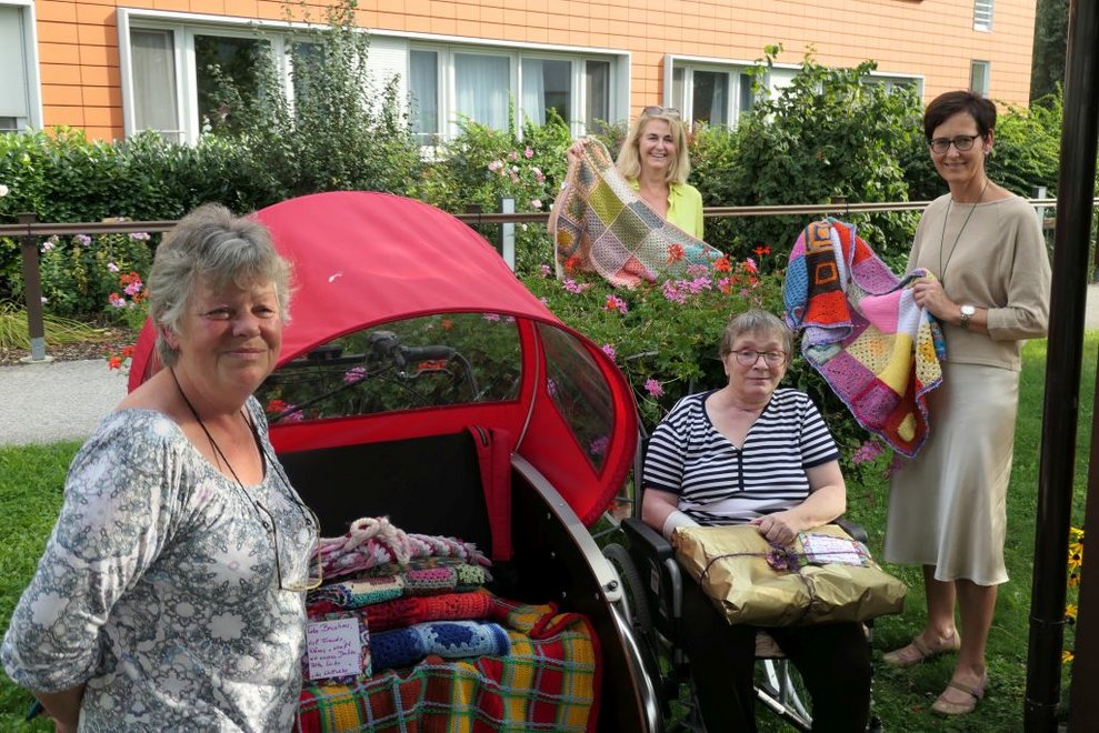 Vier Frauen mit Wolldecken vor der Rikscha im Freien.