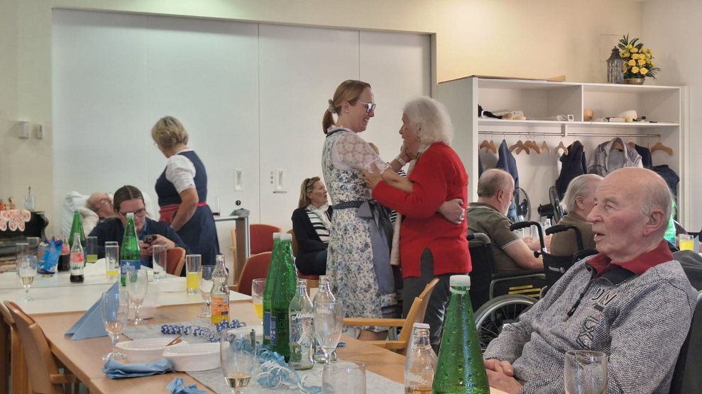 Personen beim Oktoberfest. Mitarbeiterin und Bewohnerin tanzen zusammen.